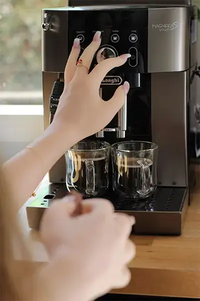 Main d’une poupée 4Woods Europe posée sur une machine à café, lumière du matin.